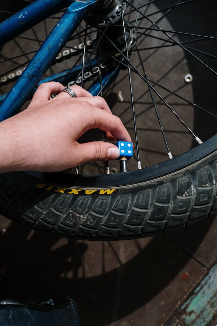 About A close-up of a hand inserting a blue dice valve cap on a bike tire outdoors.